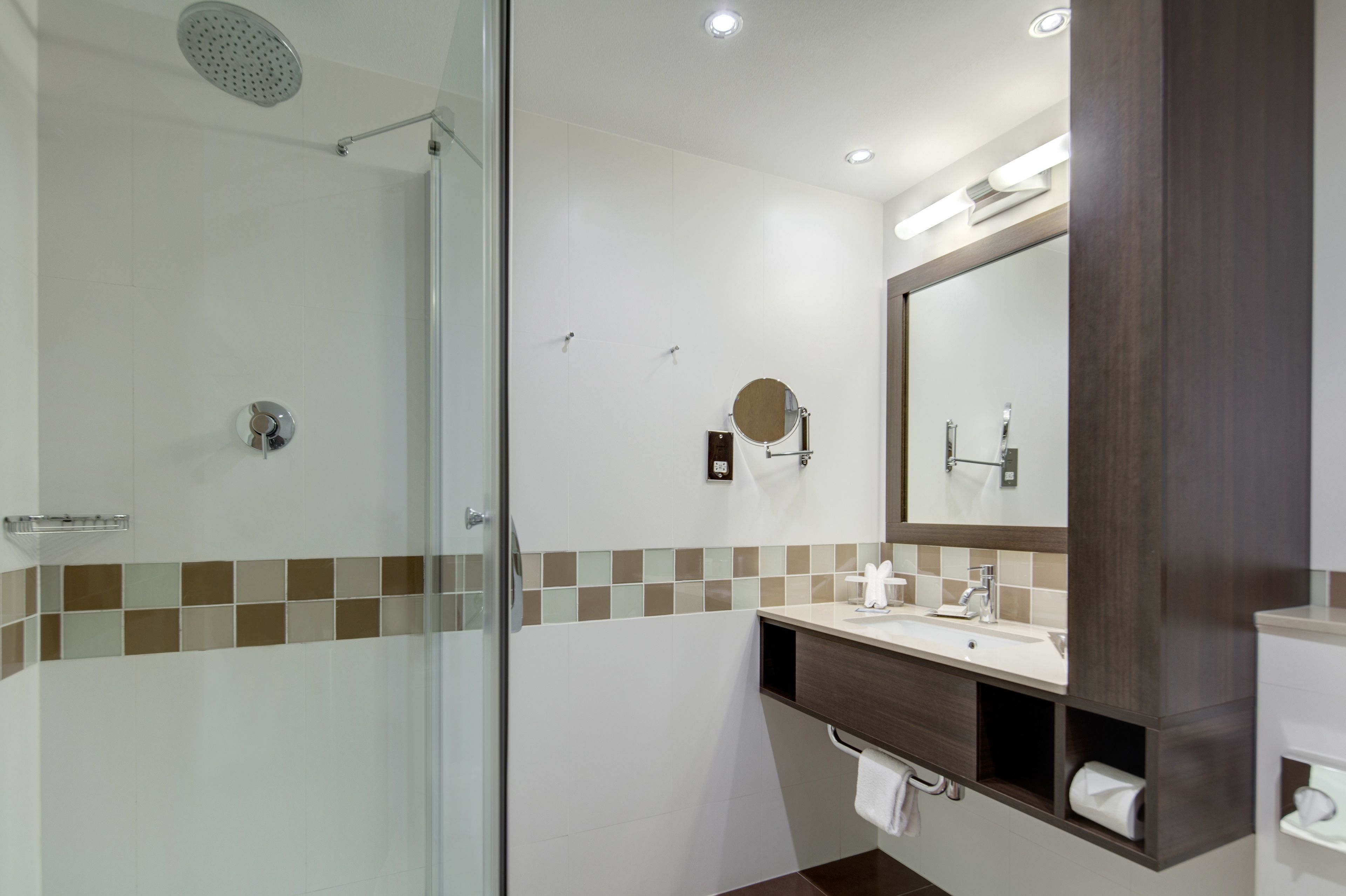 Une salle de bain moderne avec une douche à parois de verre, un grand miroir et un meuble-lavabo doté d’un porte-serviettes.