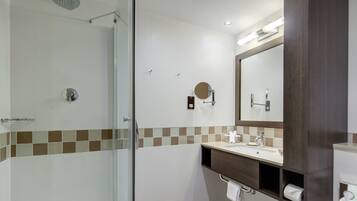 Une salle de bain moderne avec une douche à parois de verre, un grand miroir et un meuble-lavabo doté d’un porte-serviettes.