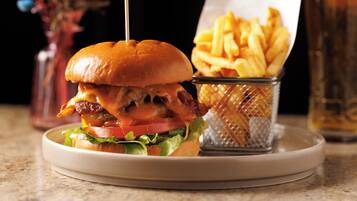 A burger with bacon, cheese, and lettuce on a bun, served with fries and a drink.