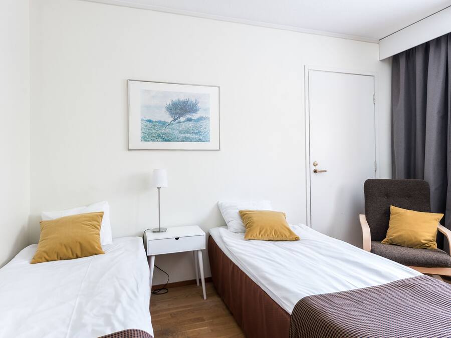 A hotel room with two single beds, a desk, a chair, a door, and a framed picture on the wall.