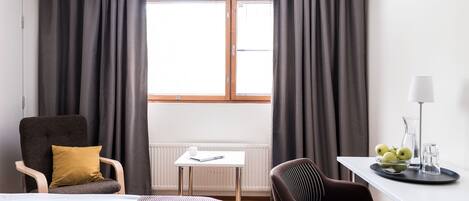 Une chambre d’hôtel avec un lit, un bureau, une chaise, un radiateur et une fenêtre avec des rideaux.
