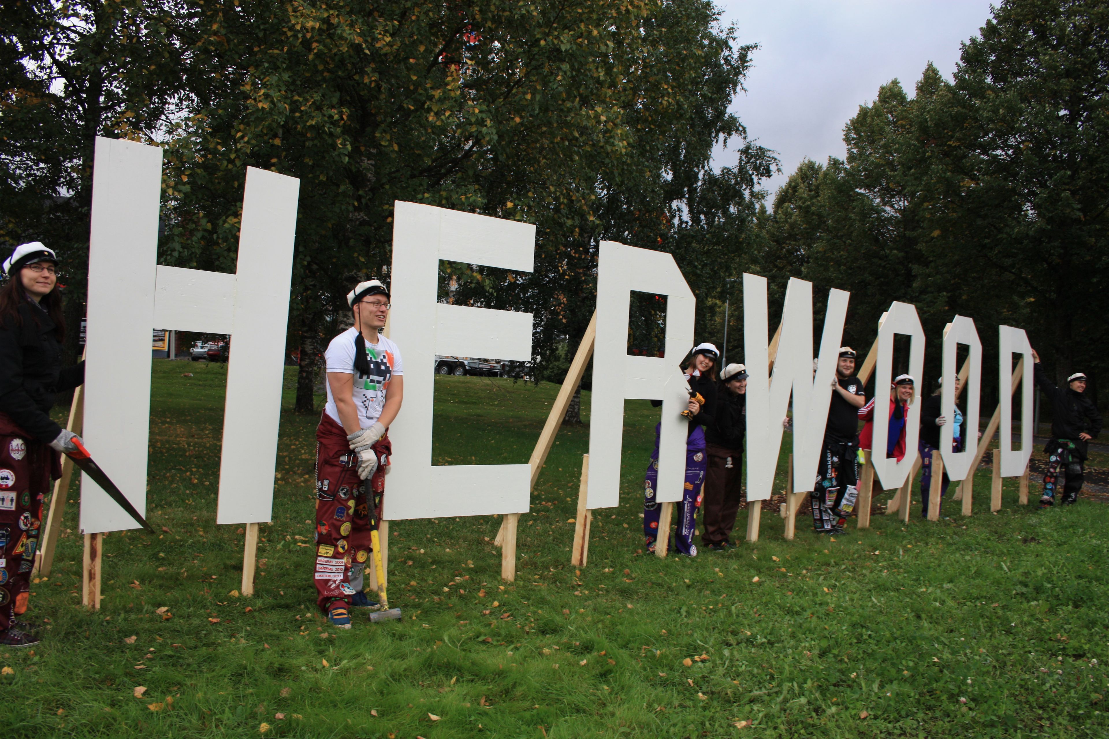 A group of people standing in front of large white letters spelling "HER WOOD".