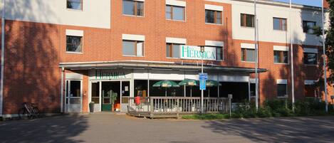 A hotel named 'Hotel Hermica' with a brick facade, a covered entrance, and outdoor seating.