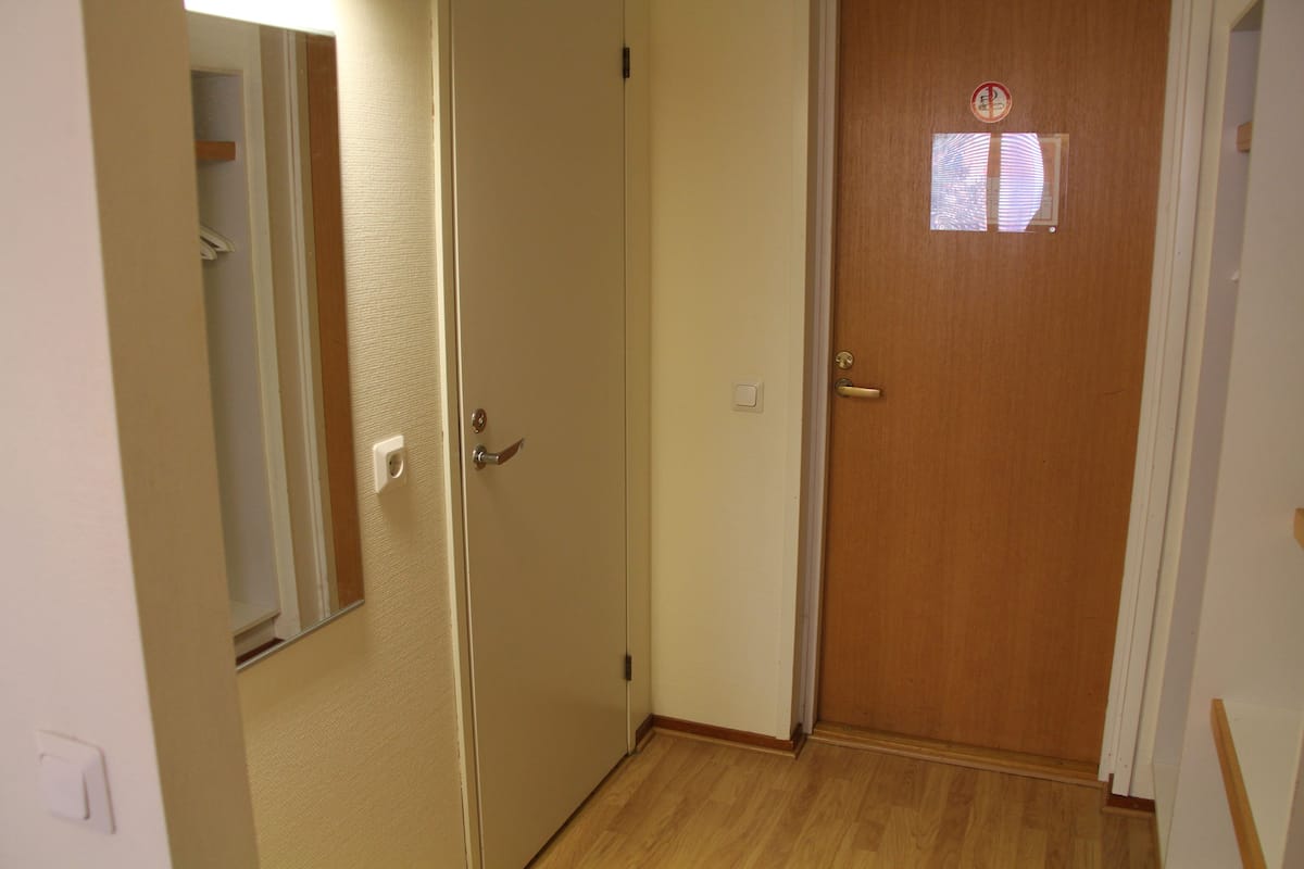 A hallway with a wooden door, a small window, and a light switch on the wall.