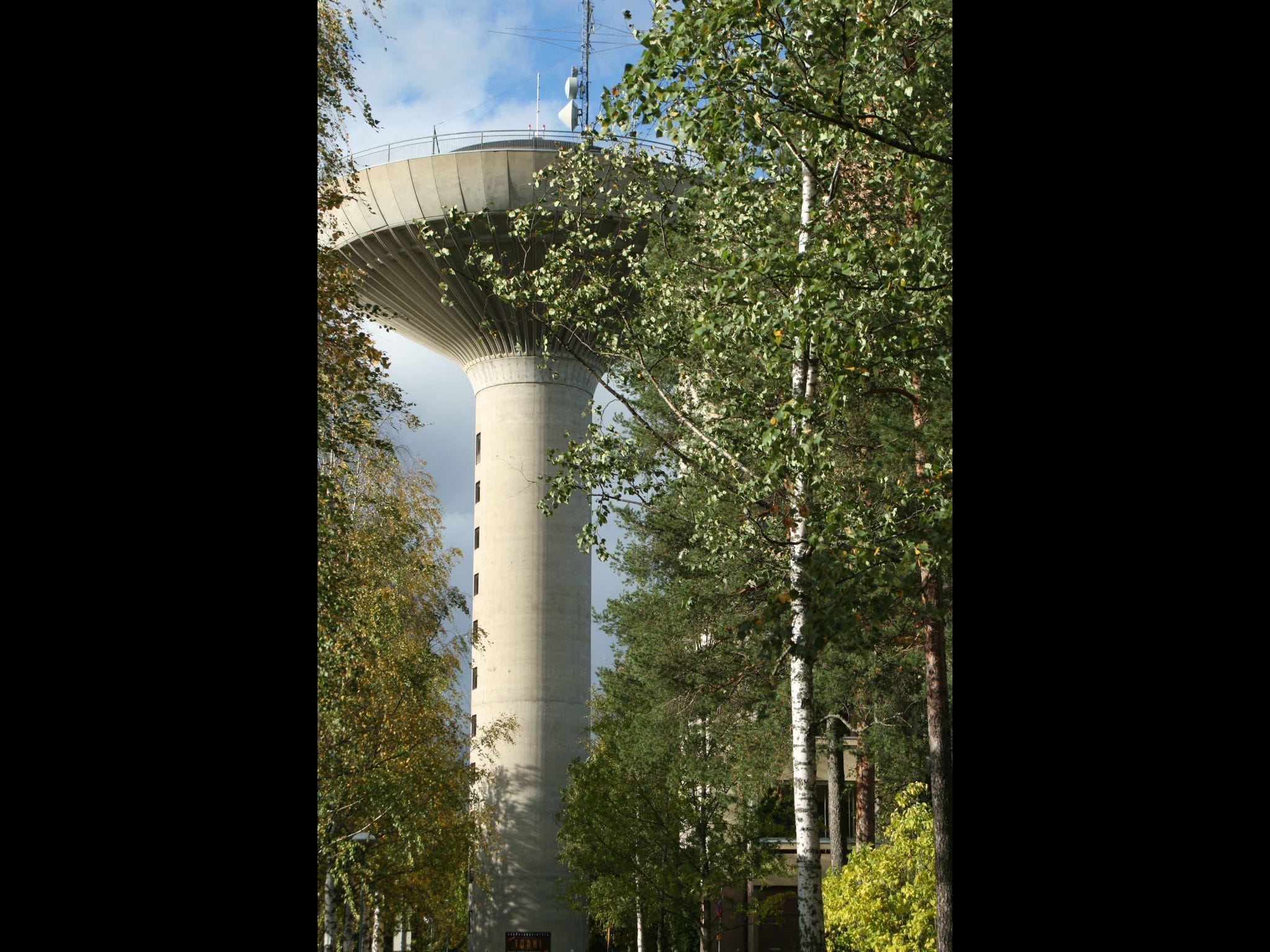 A tall, cylindrical tower with a flat top, surrounded by trees.