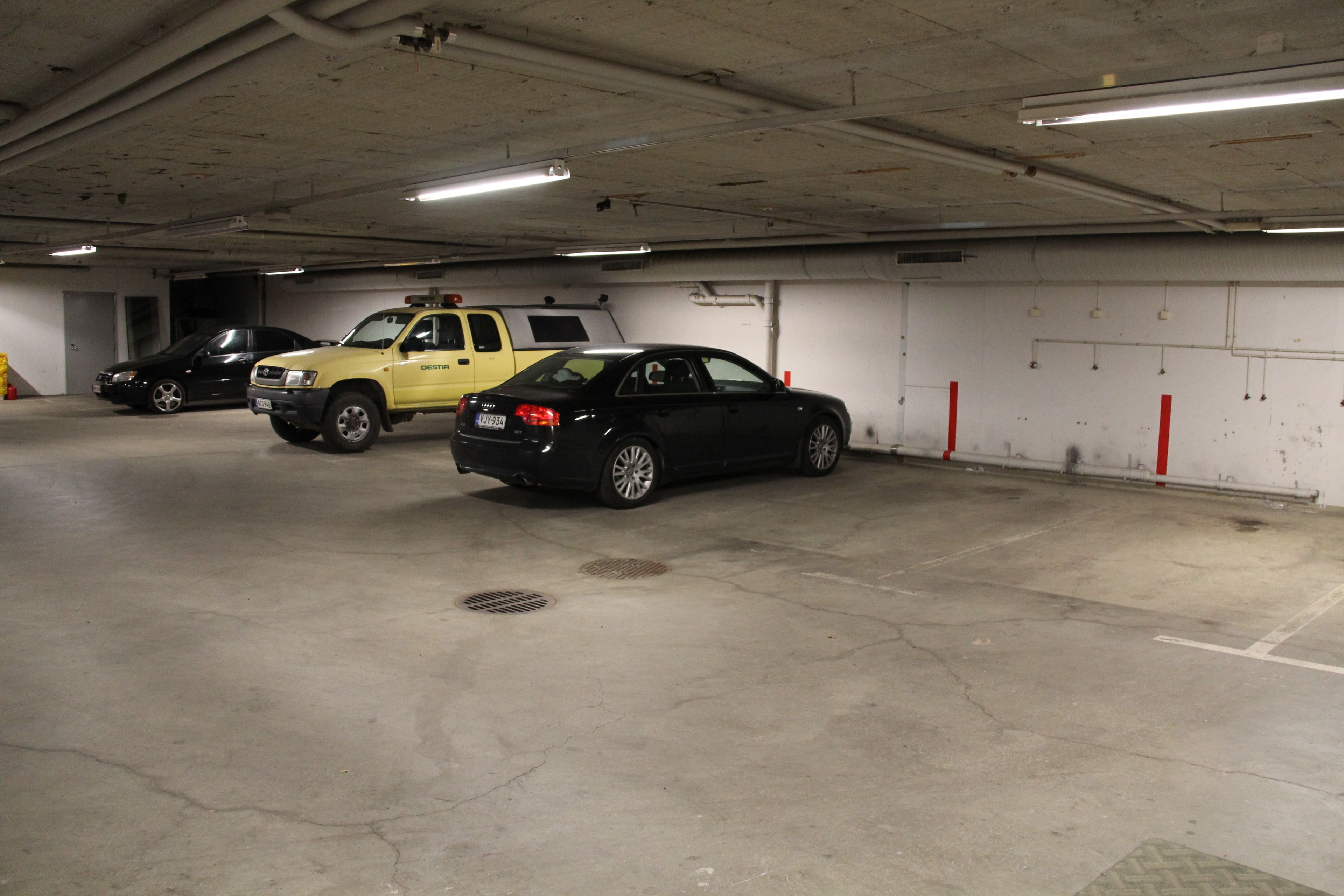 A parking garage with three vehicles: a black sedan, a yellow truck, and a black SUV.