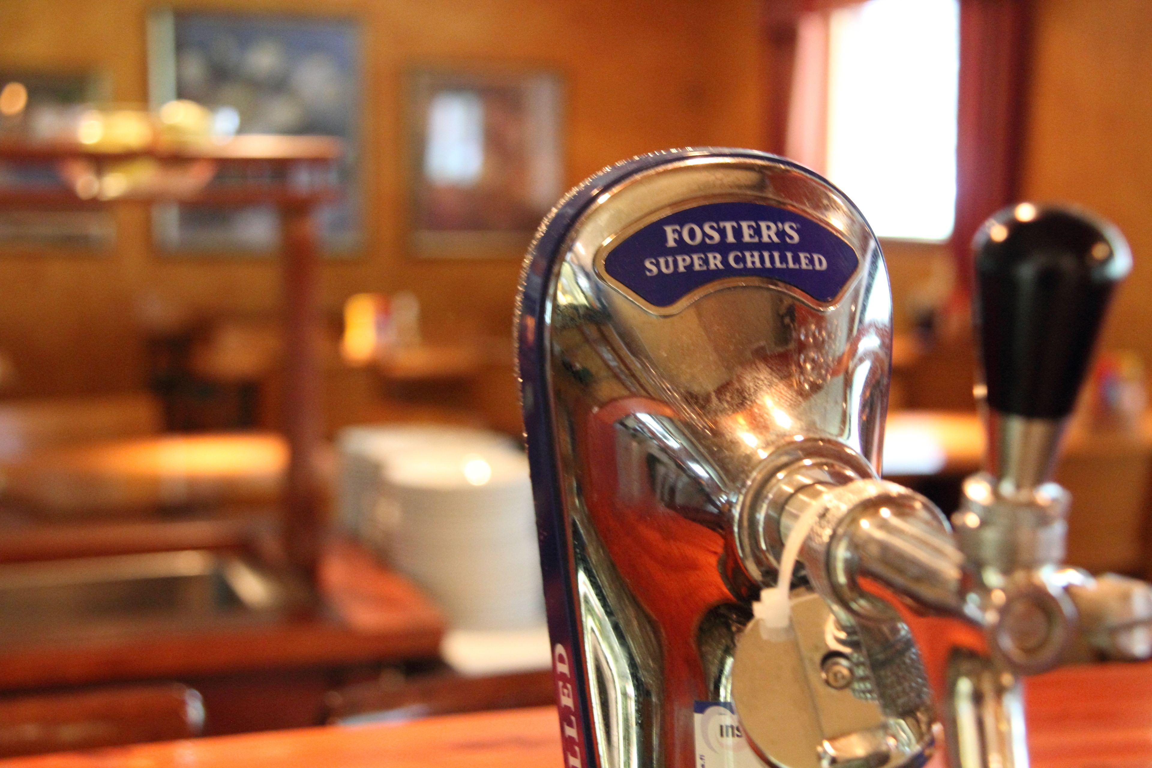A bar tap labeled "Foster's Super Chilled" with a beer pump and a wooden bar counter in the background.
