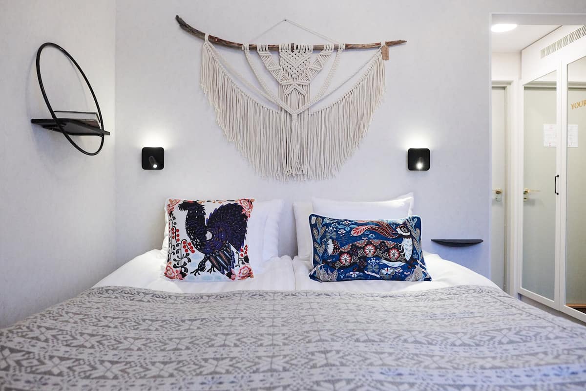 A neatly made bed with patterned bedding, a macrame wall hanging, and a wall-mounted shelf.