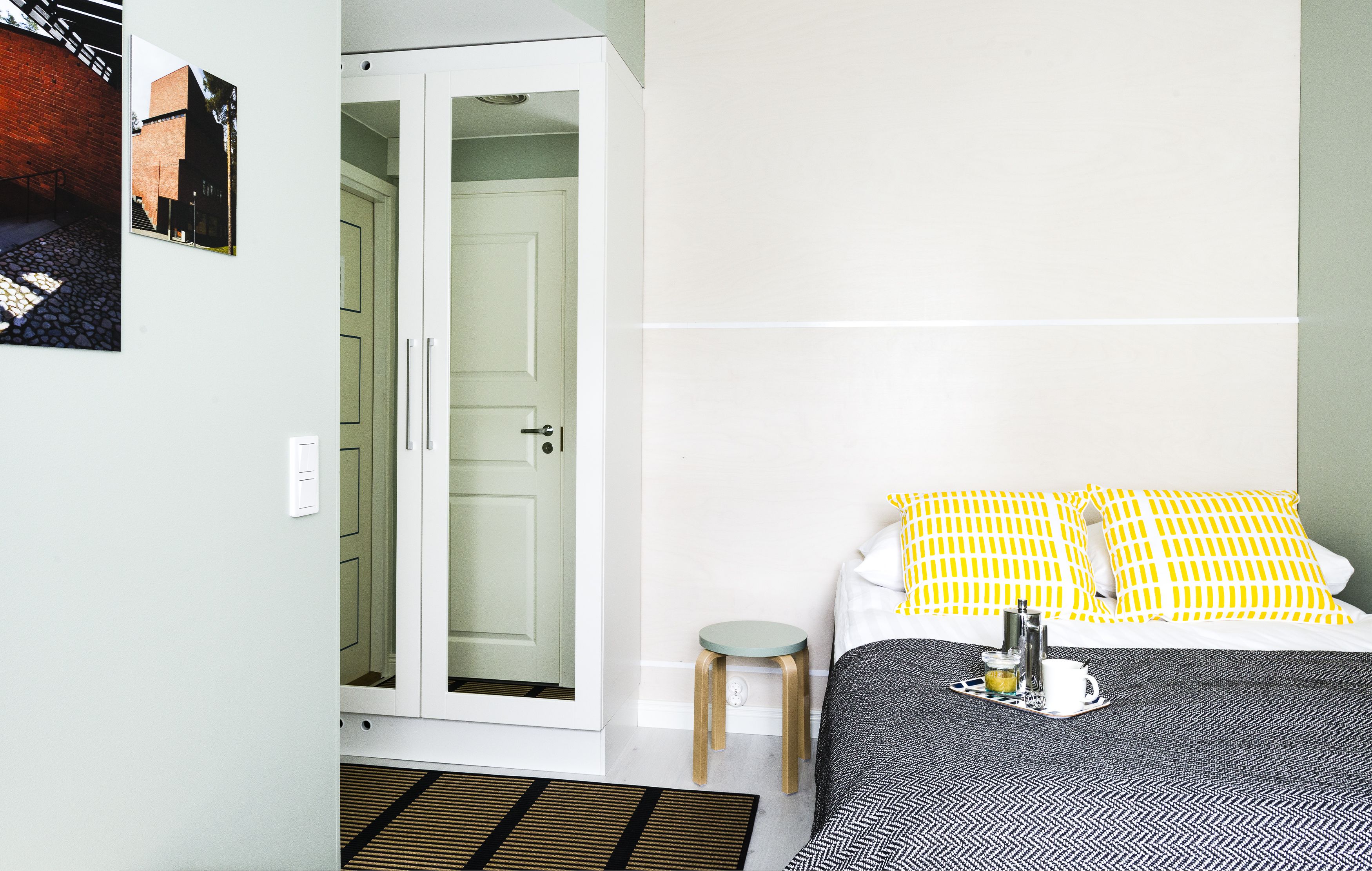 A bedroom with a bed, a bedside table, a small stool, a wardrobe, and a door.