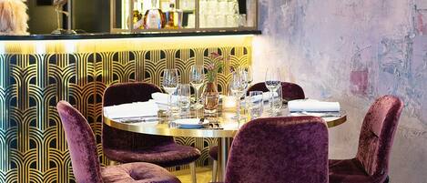 A dining area with a round table, purple velvet chairs, and a chandelier.