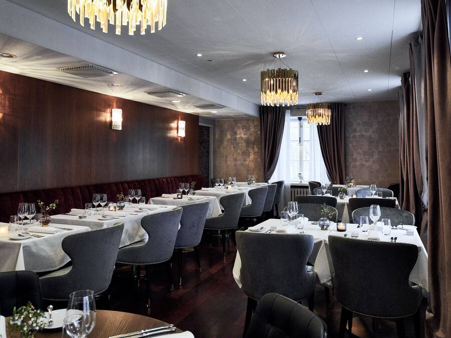 A restaurant with multiple tables set for dining, featuring a modern interior with wooden paneling and contemporary lighting fixtures.