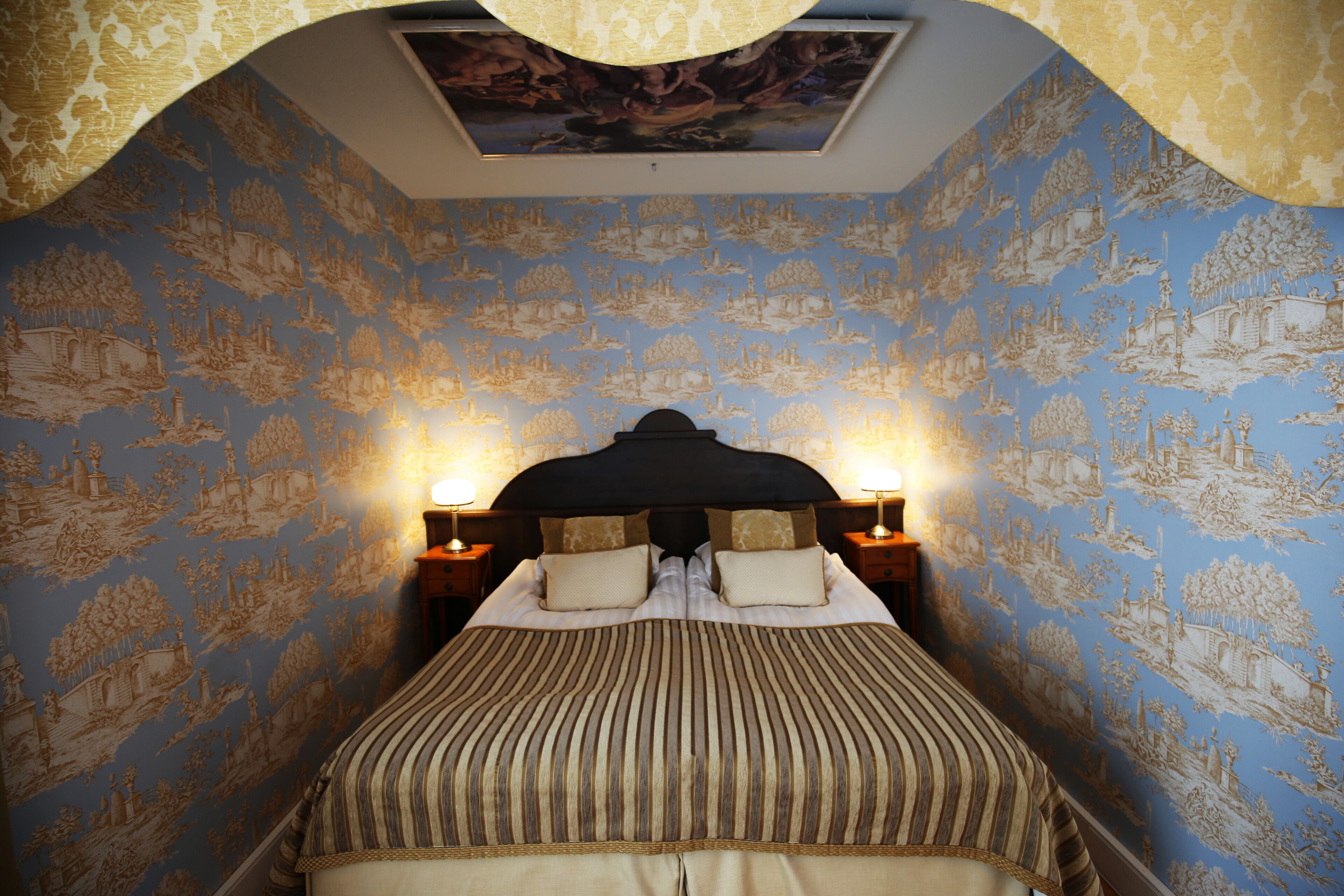 Ein Schlafzimmer mit einem großen Bett, aufwendiger Tapete und zwei Nachttischlampen.