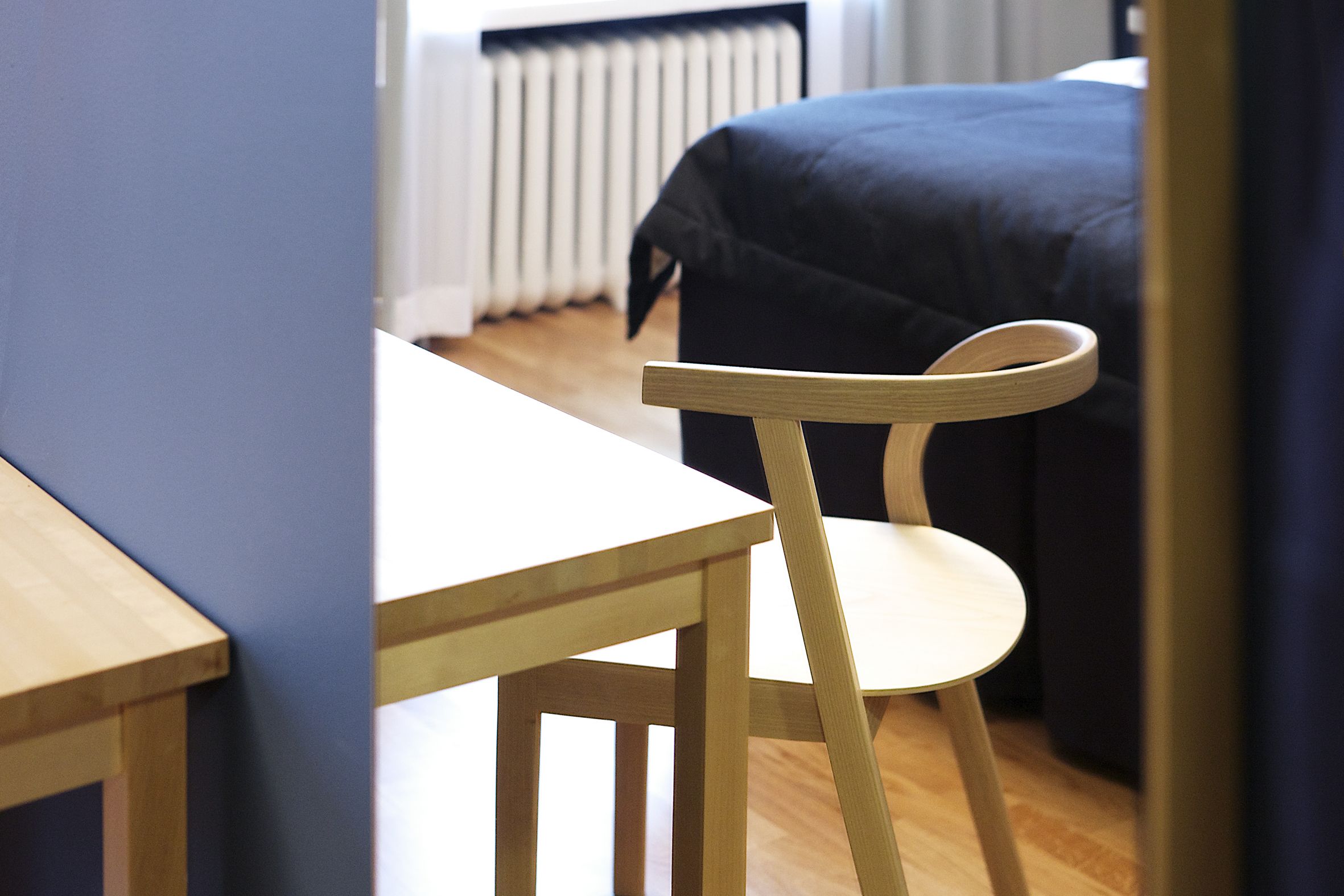 Una sedia e un tavolo in legno in una stanza con un letto e un termosifone sullo sfondo.