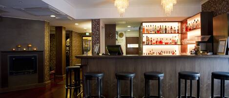 A bar area with a wooden counter, bar stools, and a variety of bottles and glasses.