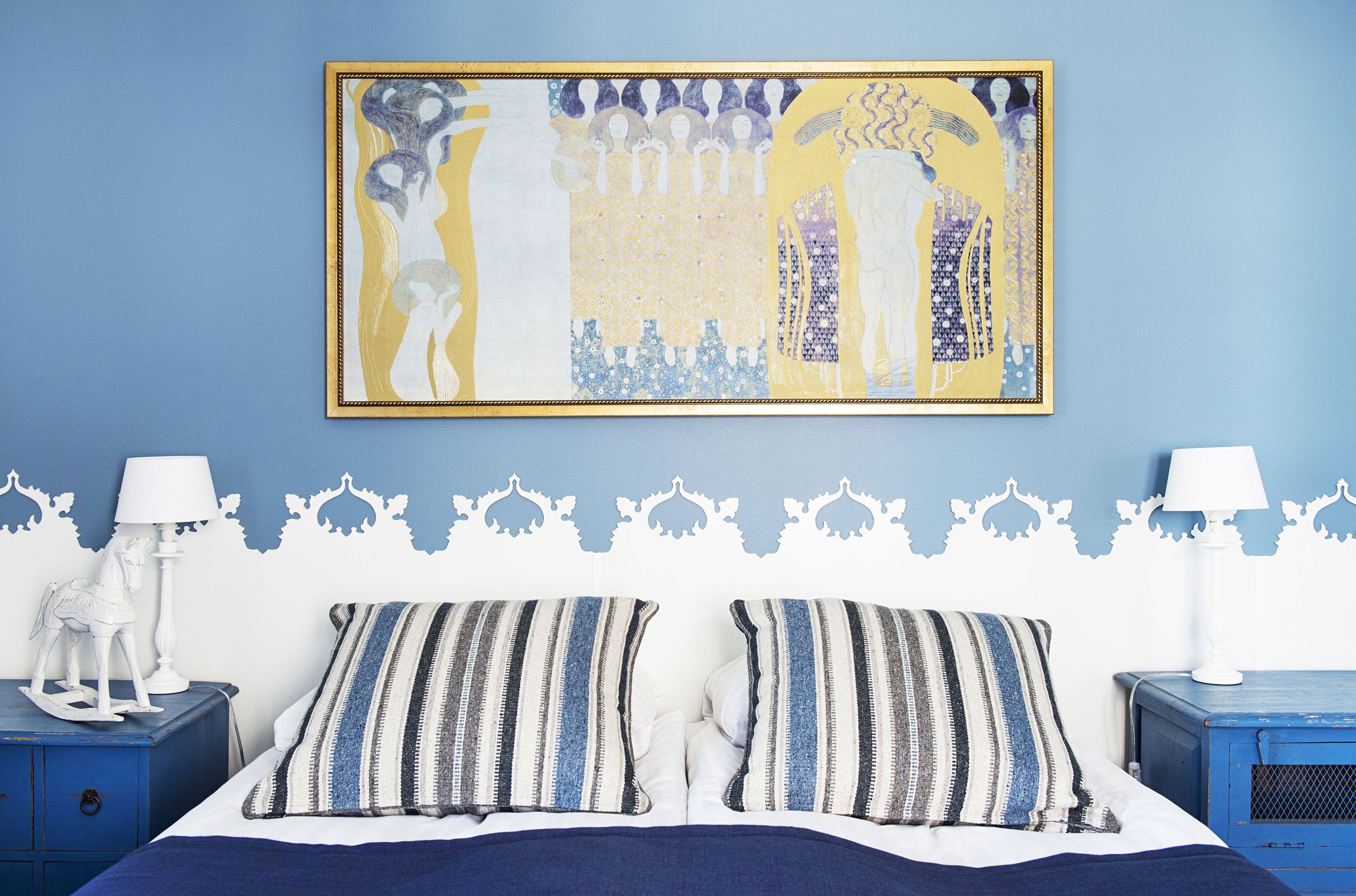 A bedroom with a bed, two nightstands, a wall-mounted painting, and decorative wall trim.