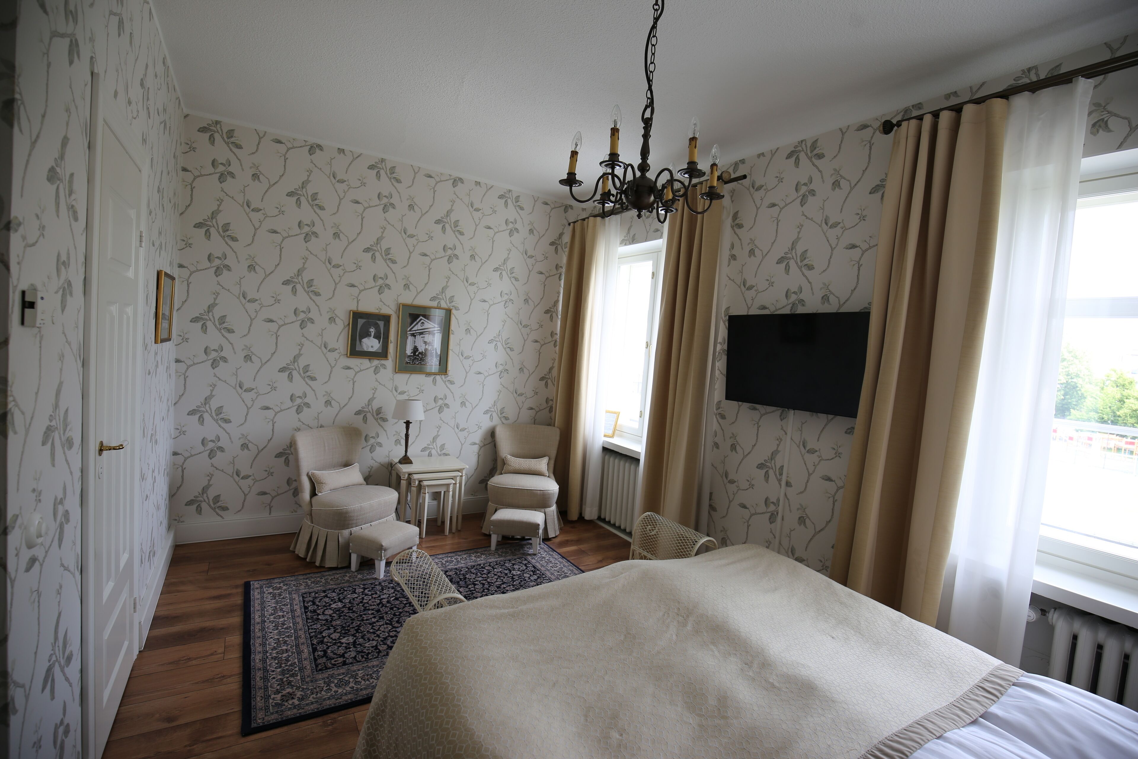 Une chambre avec un grand lit, une chaise, une petite table et un téléviseur fixé au mur.