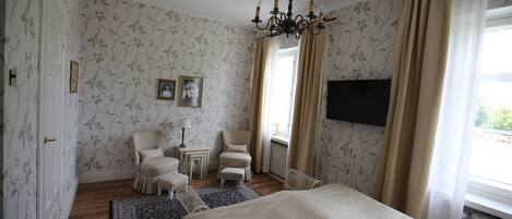 Une chambre avec un grand lit, une chaise, une petite table et un téléviseur fixé au mur.