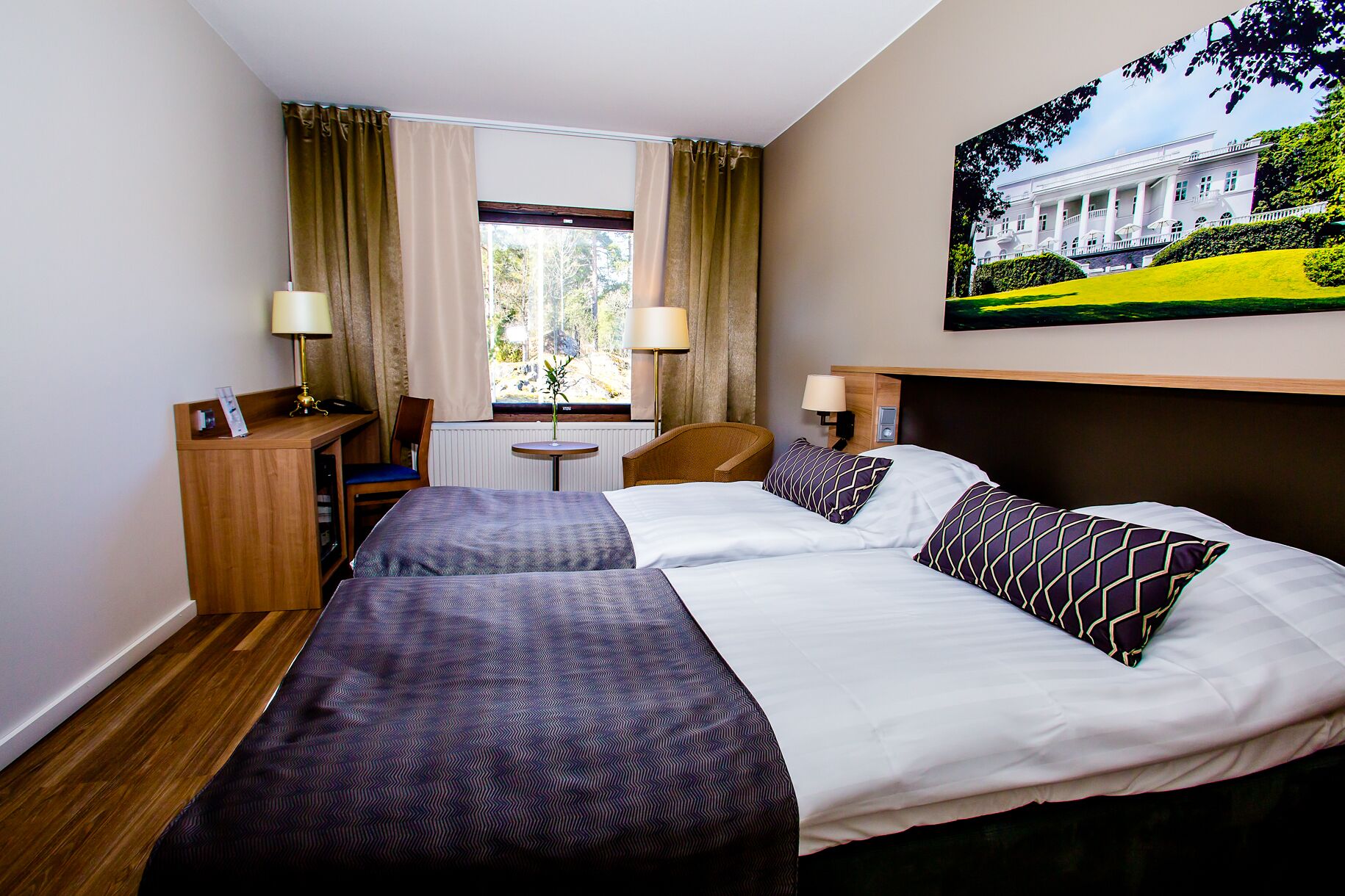 A hotel room with two beds, a desk, a chair, a small table, and a window with curtains.