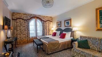 A hotel room with a large bed, a sofa, a desk, and a chandelier.