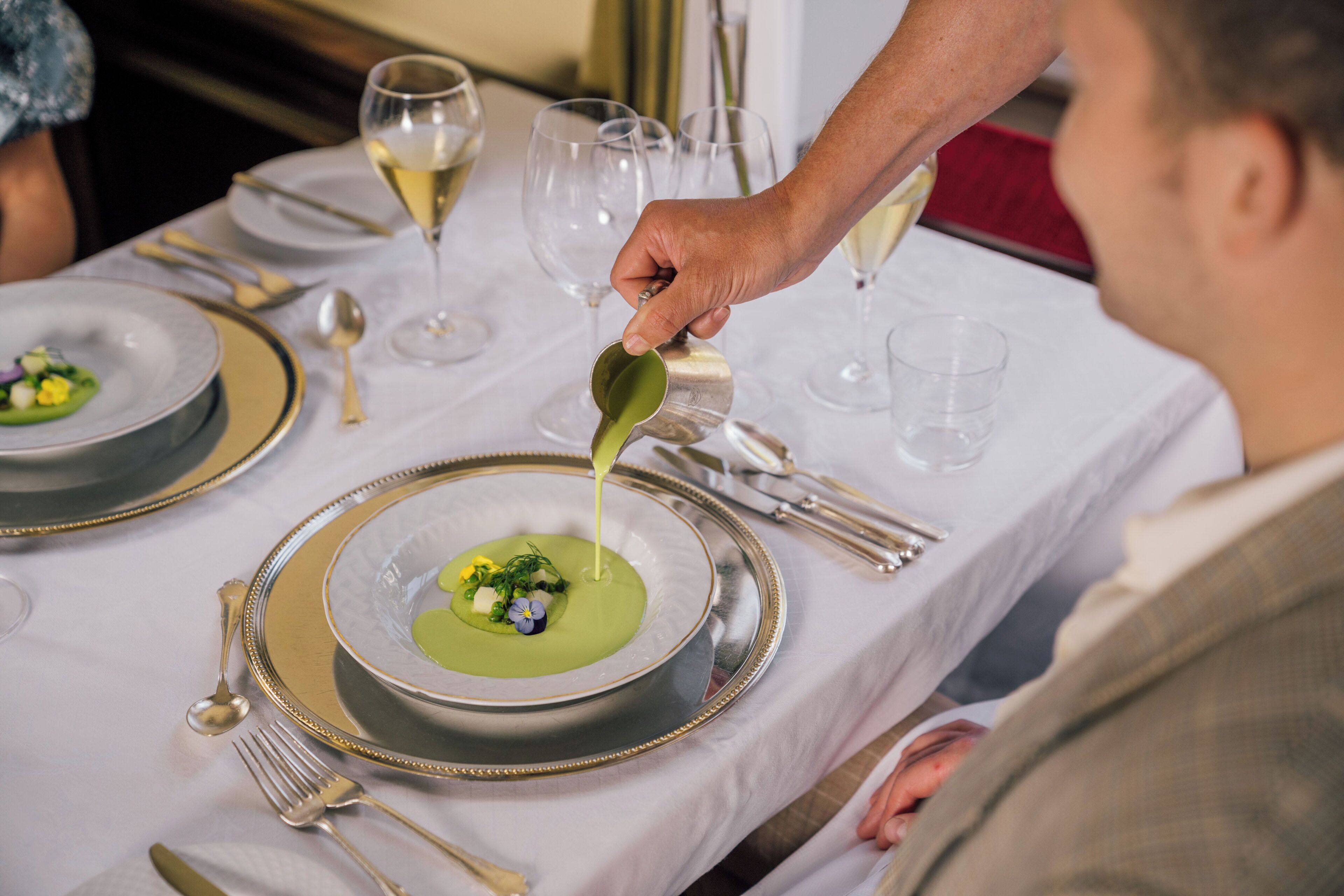 Una mesa de comedor con mantel blanco, un tazón de sopa y una cuchara.