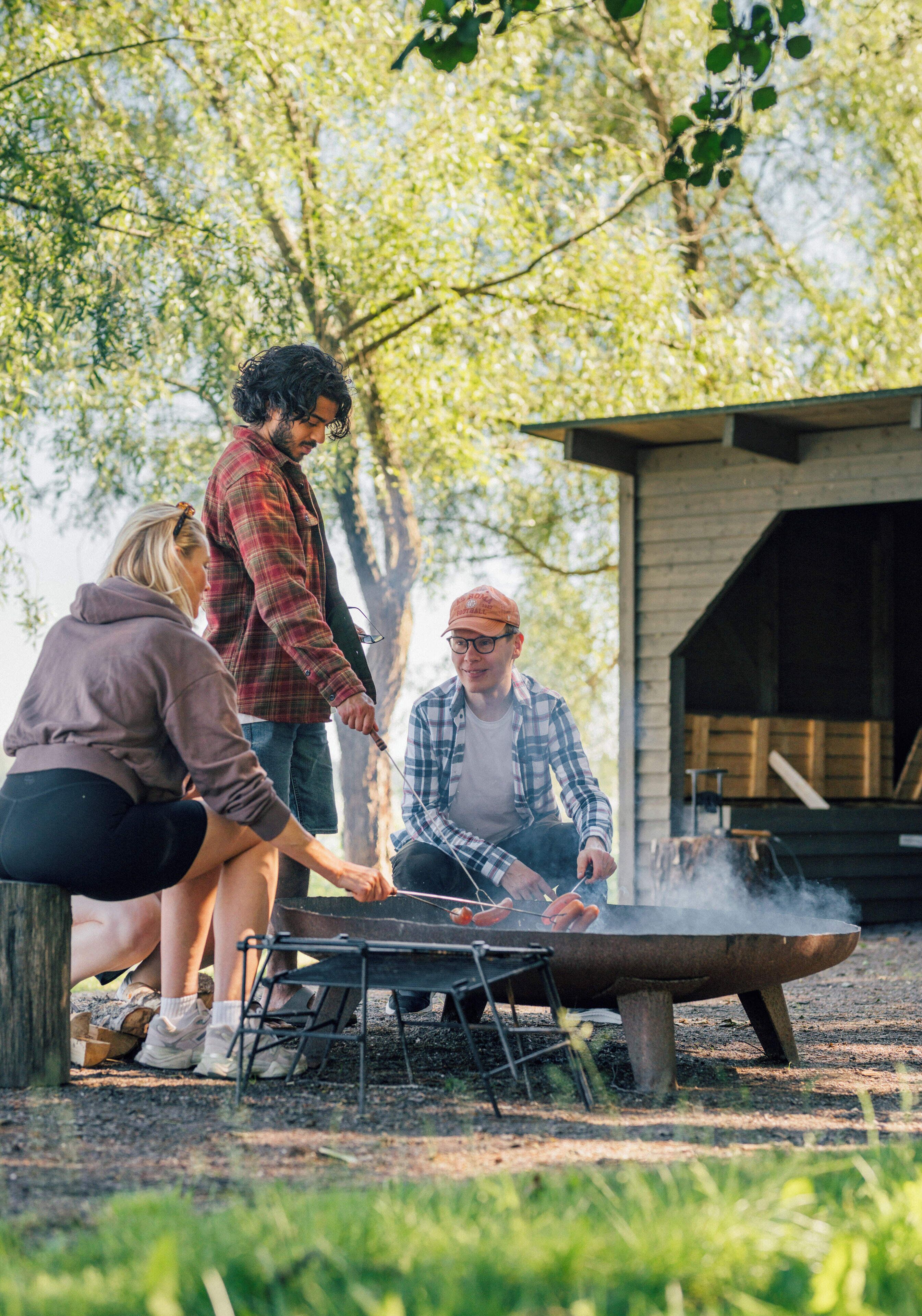 A group of people around an outdoor grill with a wooden structure in the background.