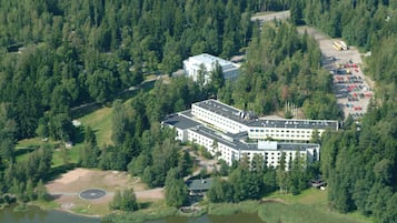 A large hotel with multiple buildings, surrounded by dense forest and a body of water.