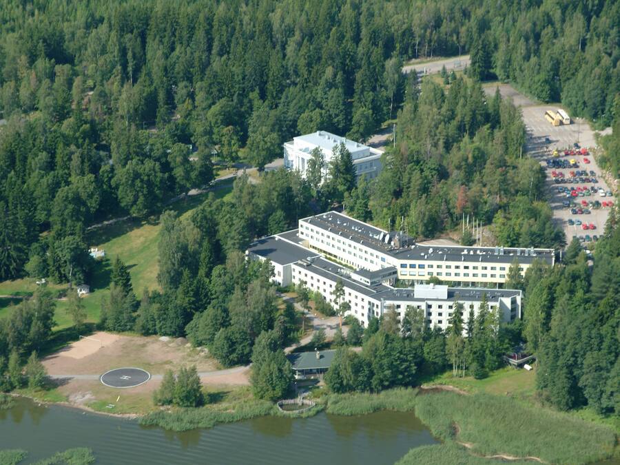 A large hotel with multiple buildings, surrounded by dense forest and a body of water.