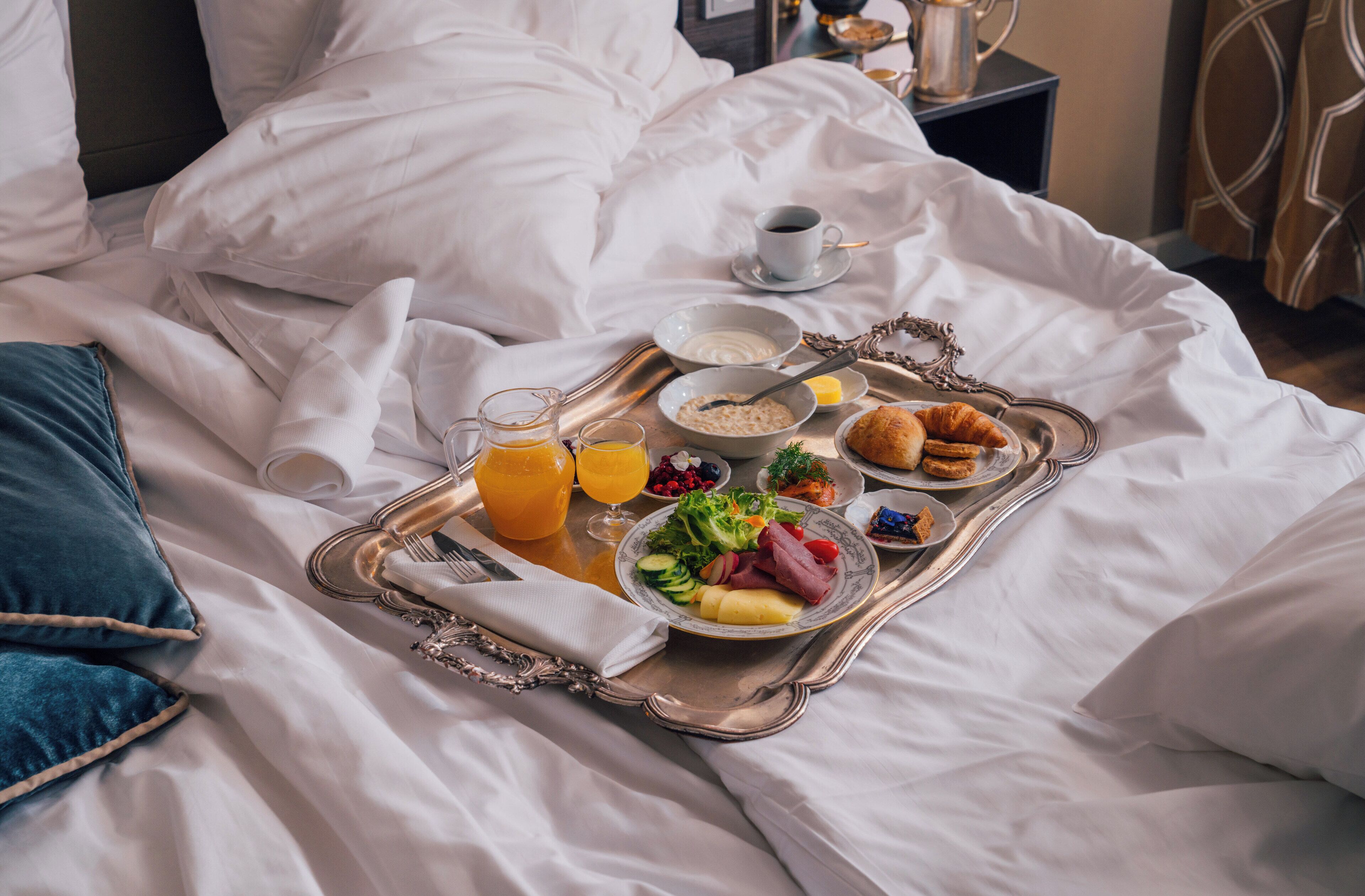 A neatly made bed with a tray of breakfast items including cereal, fruit, eggs, and pastries.