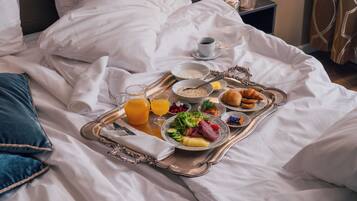 A neatly made bed with a tray of breakfast items including cereal, fruit, eggs, and pastries.