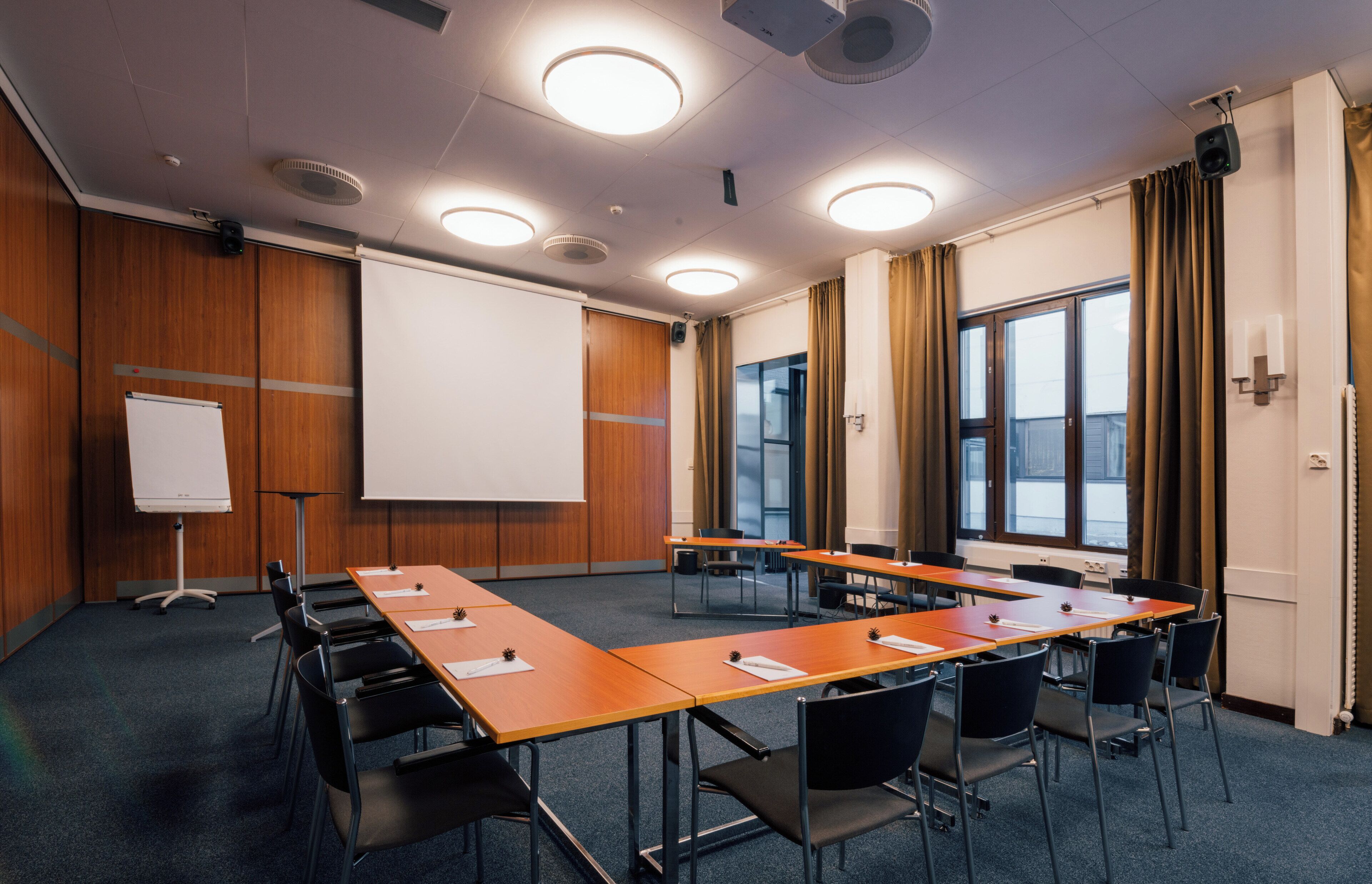 Un salón de conferencias con una larga mesa, sillas, una pizarra y una pantalla para proyector.