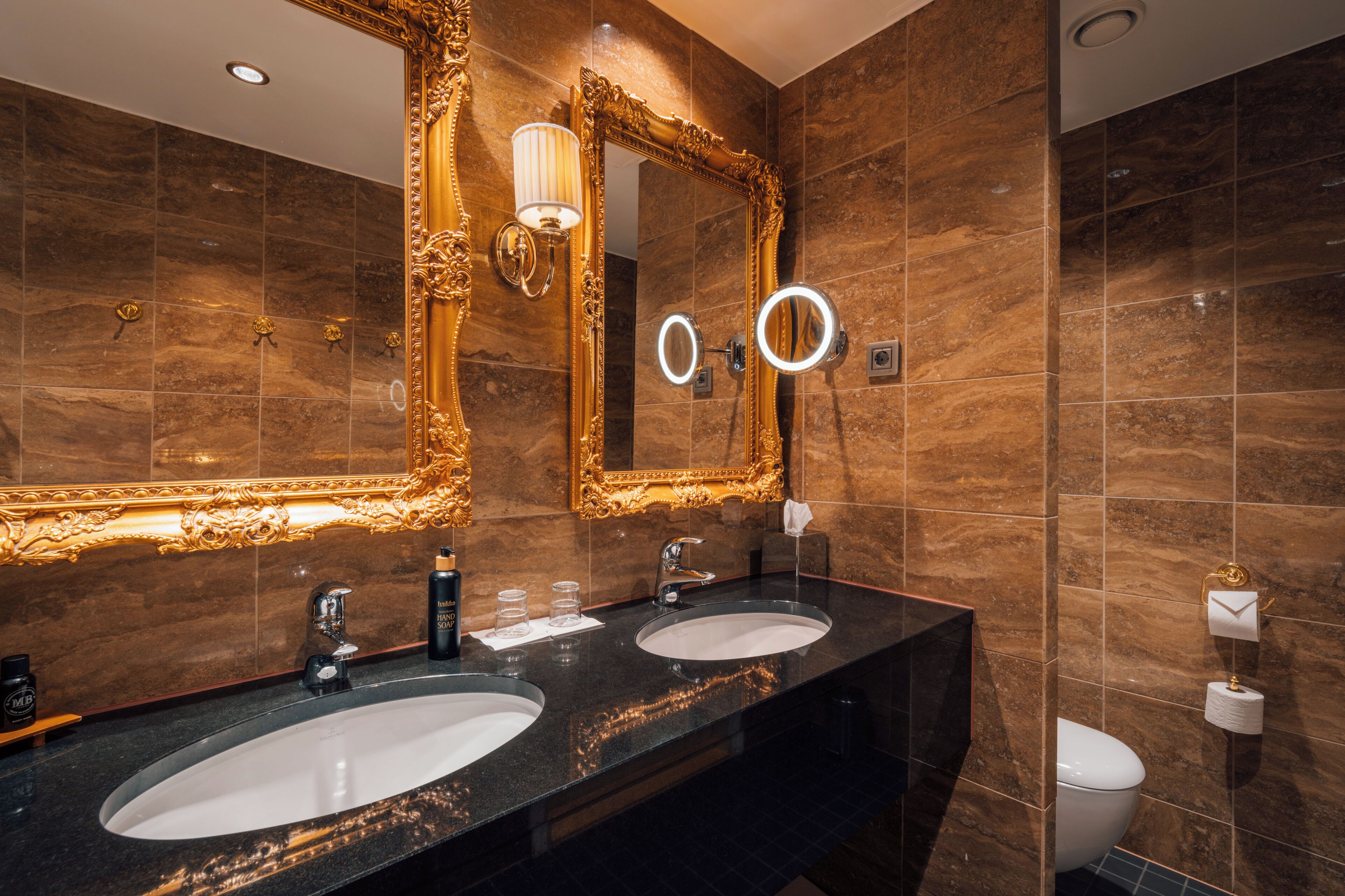 A bathroom with two sinks, a large ornate mirror, and a toilet.