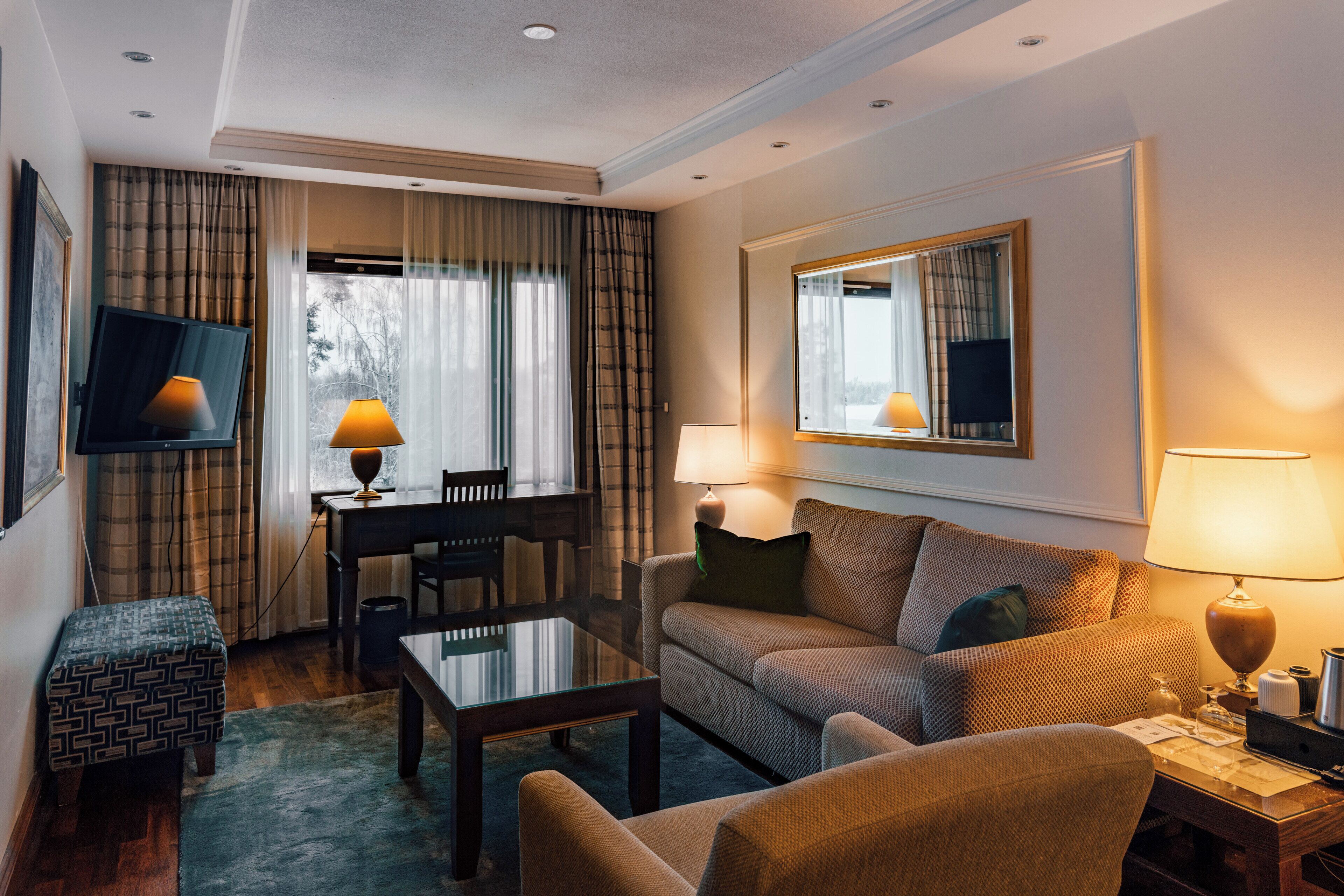 Une chambre d’hôtel équipée d’un canapé, d’un fauteuil, d’une table à manger et d’un téléviseur fixé au mur.