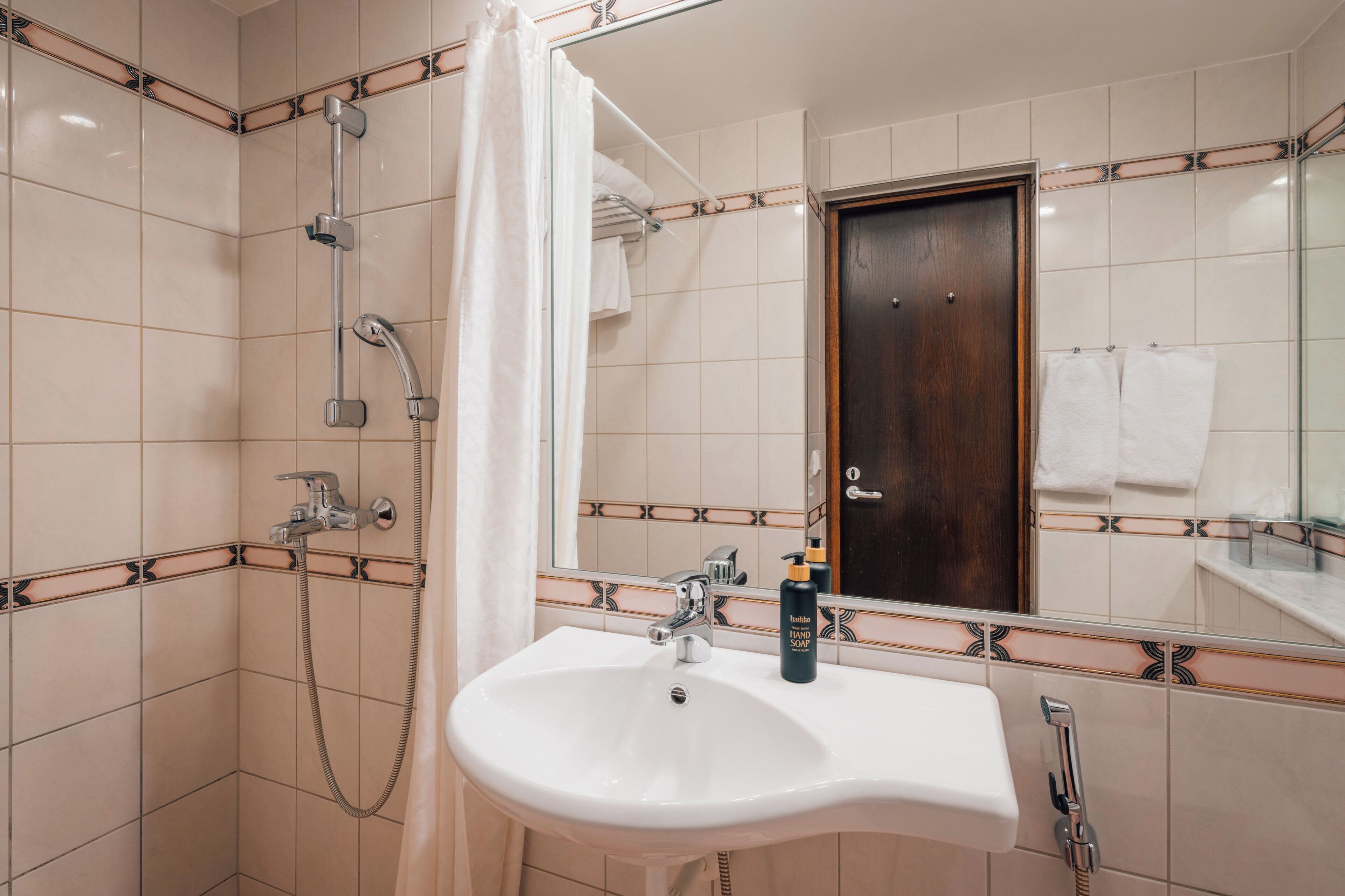 A bathroom with a white sink, a shower with a curtain, a wooden door, and a mirror.