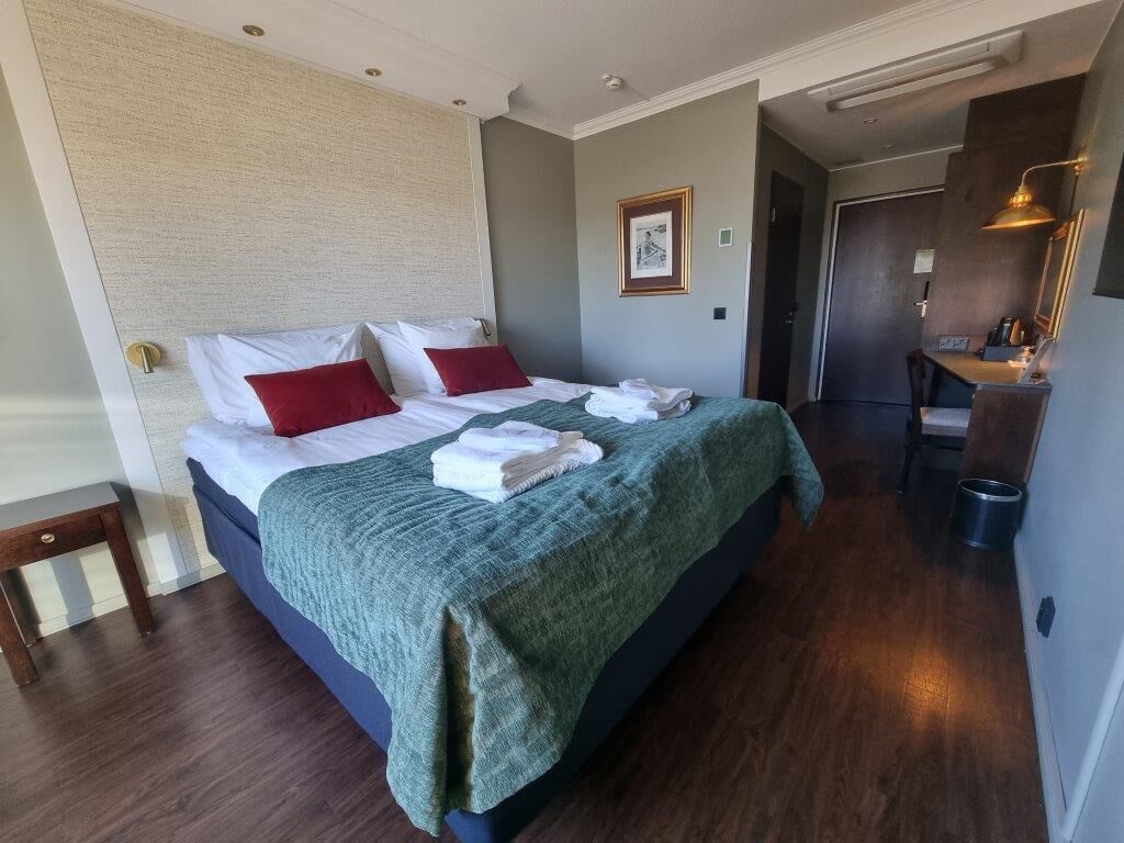 A hotel room with a large bed, a desk, and a mirror.