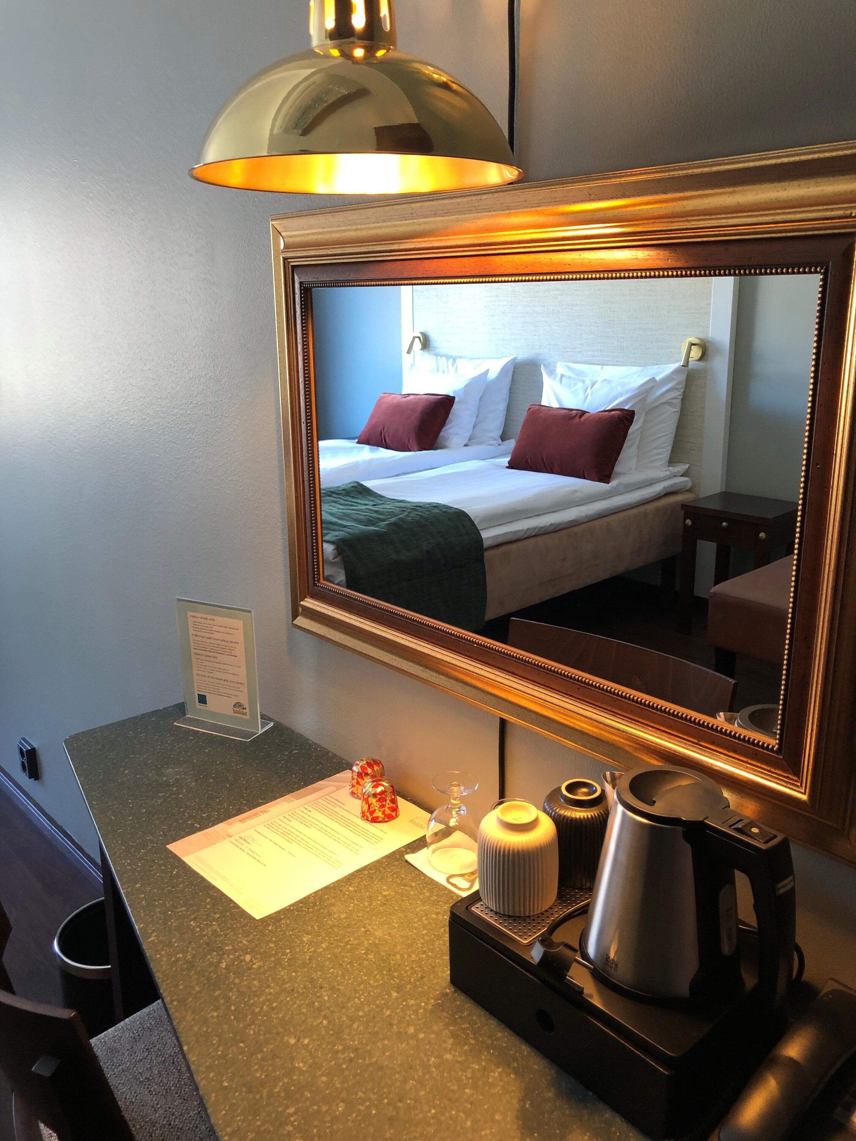 Una habitación de hotel con cama, espejo, cafetera y una pequeña mesa con un menú.