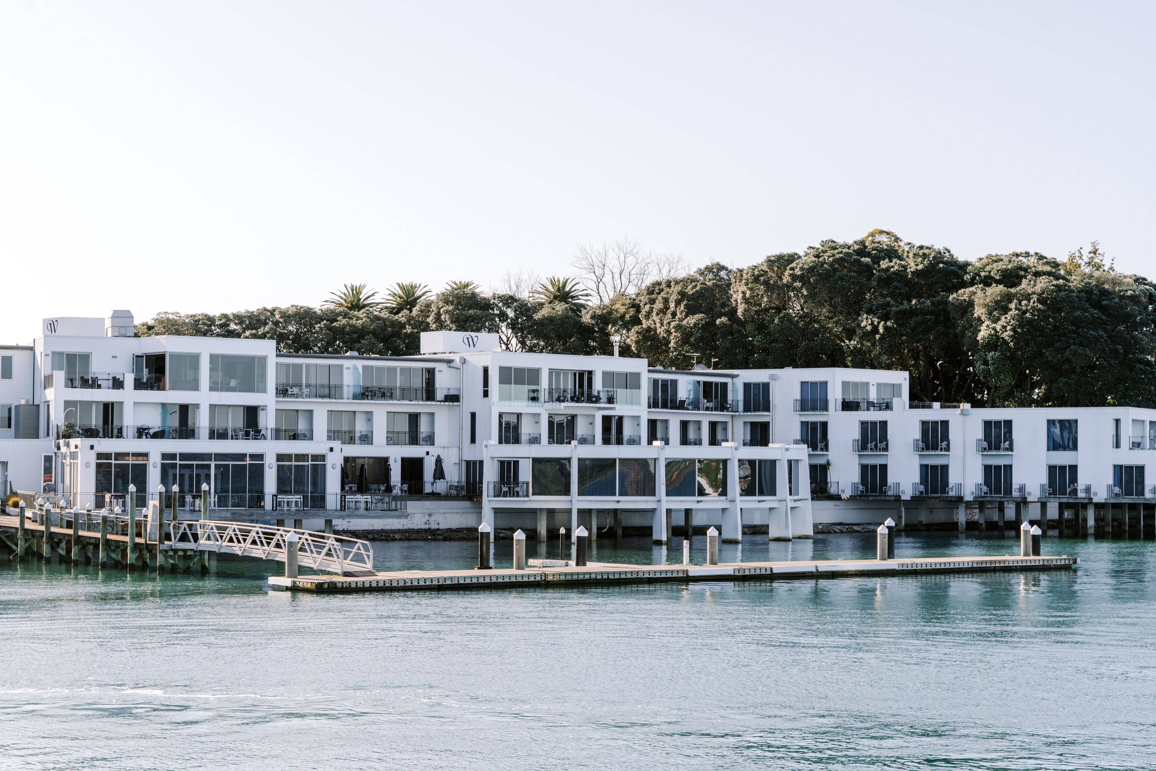 A waterfront hotel with multiple white buildings, a dock, and a bridge.