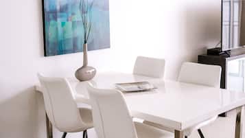 Een moderne eetruimte met een witte tafel en stoelen, een vaas met takken en een wandairconditioner.