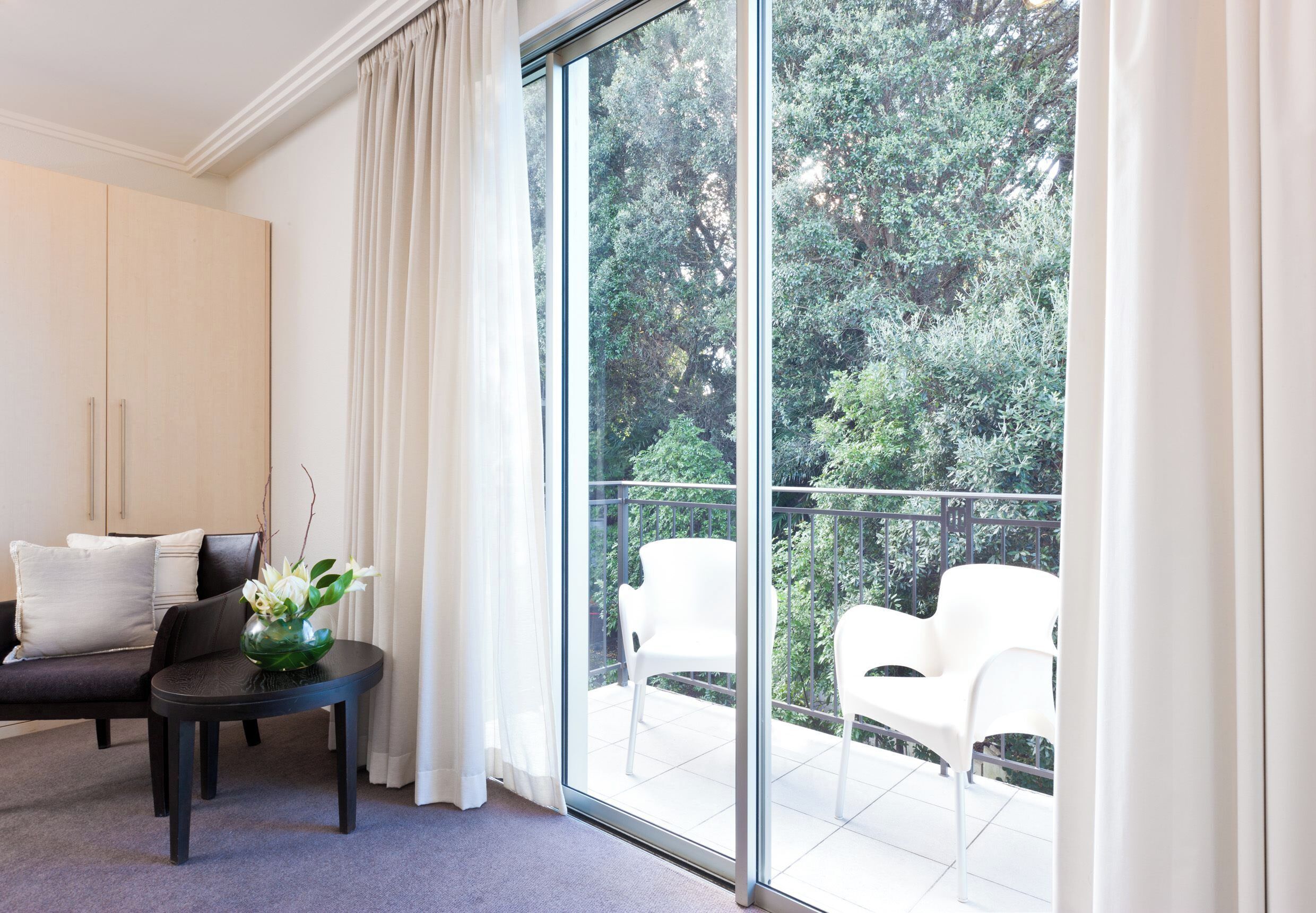 A modern room with a large sliding glass door leading to a balcony with white chairs.