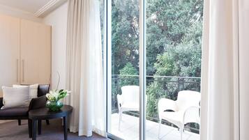 Una habitación moderna con un amplio ventanal corredero que da a un balcón con sillas blancas.