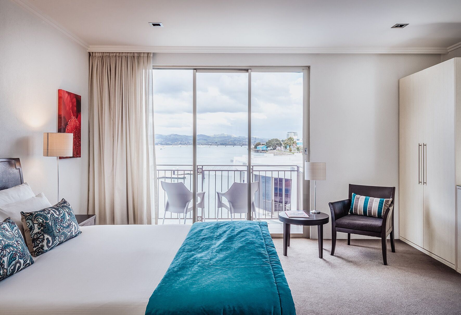 A hotel room with a large bed, a balcony with chairs, and a view of the sea.