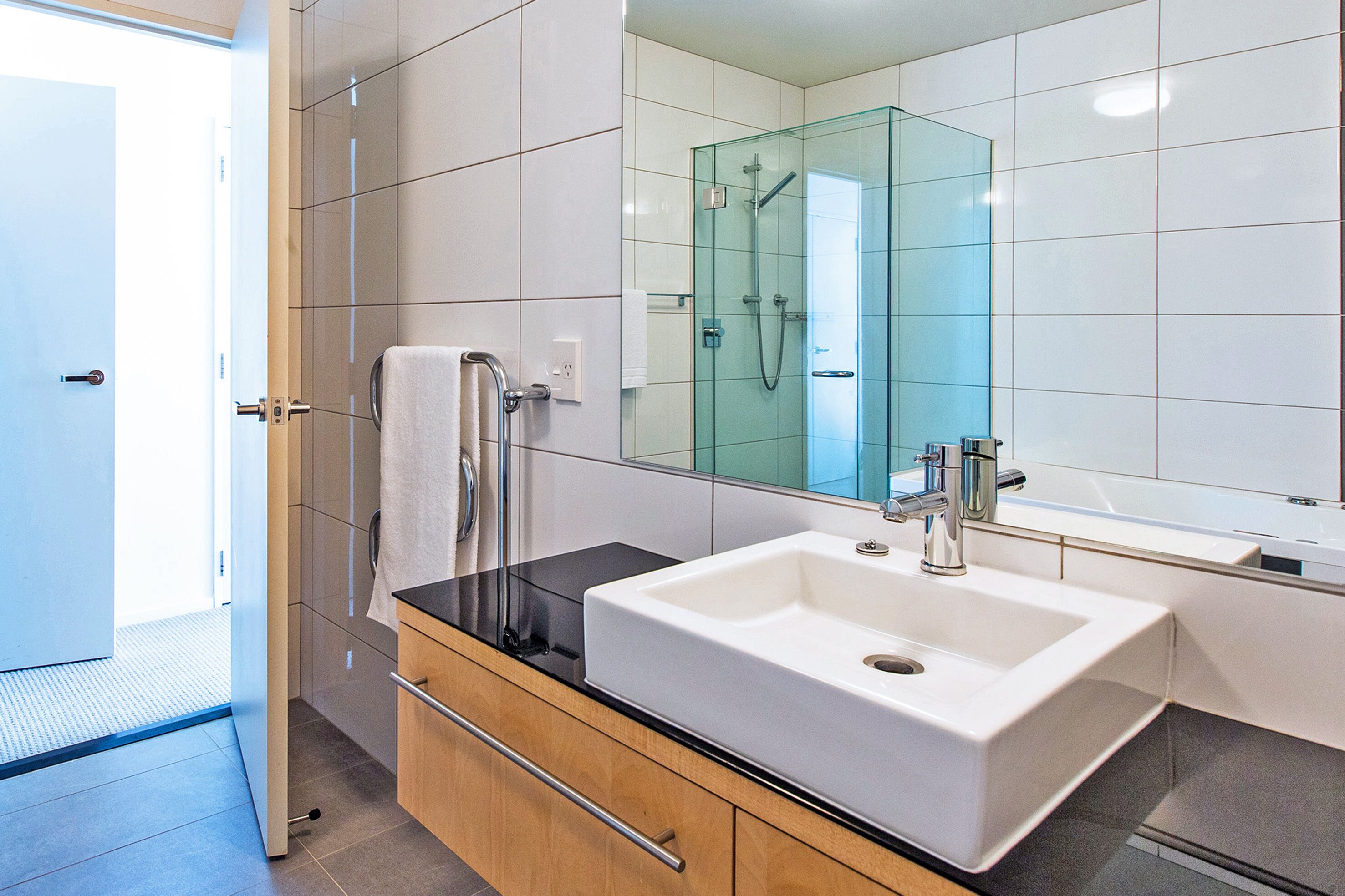 Un baño moderno con un espejo grande, un lavamanos blanco y una ducha con mampara de vidrio.