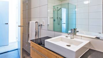 Un baño moderno con un espejo grande, un lavamanos blanco y una ducha con mampara de vidrio.