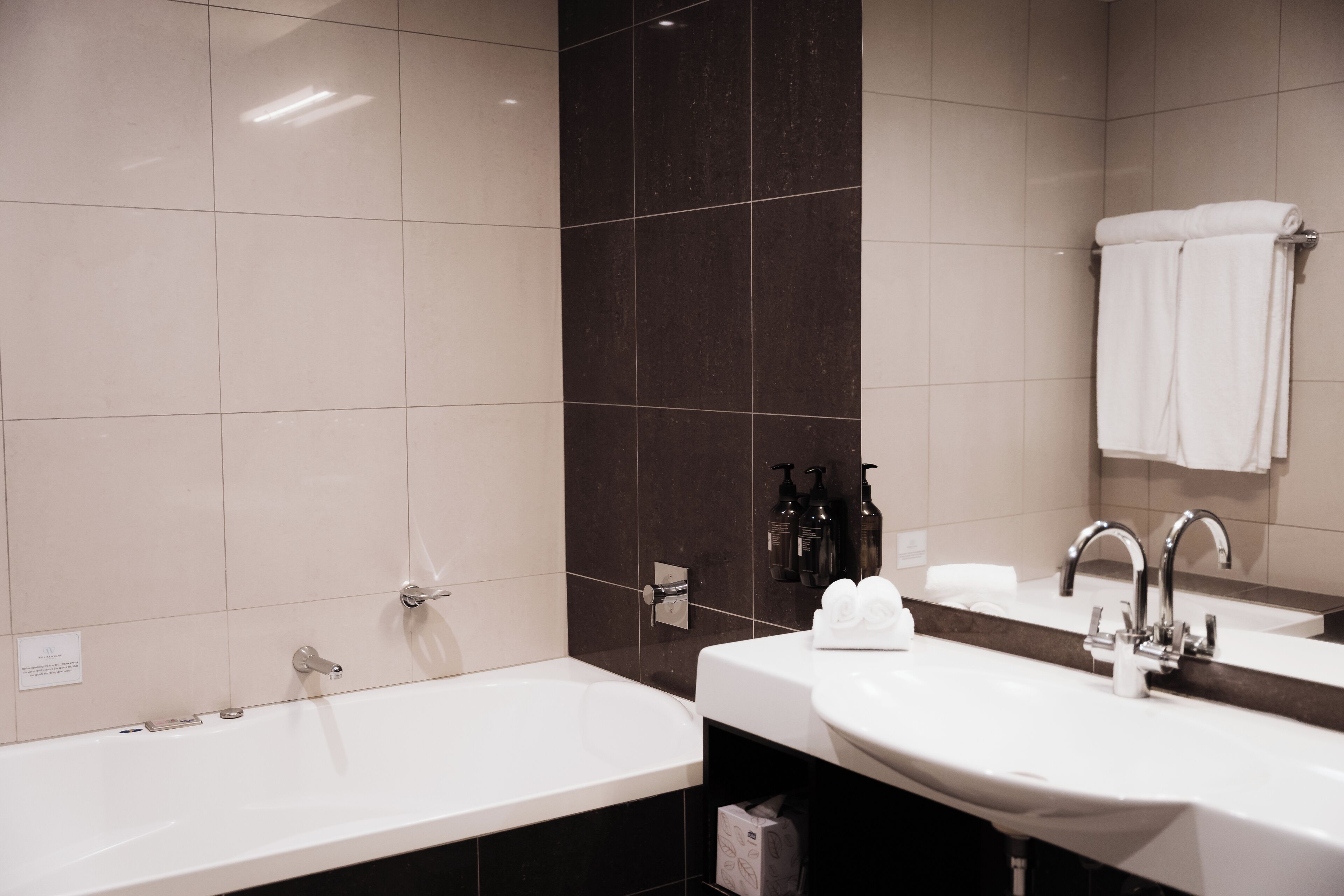 Um banheiro moderno com uma banheira grande, duas pias e uma parede revestida de azulejos escuros.