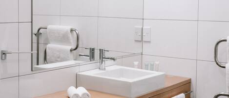 A modern bathroom with a white sink, wooden vanity, and a mirror.