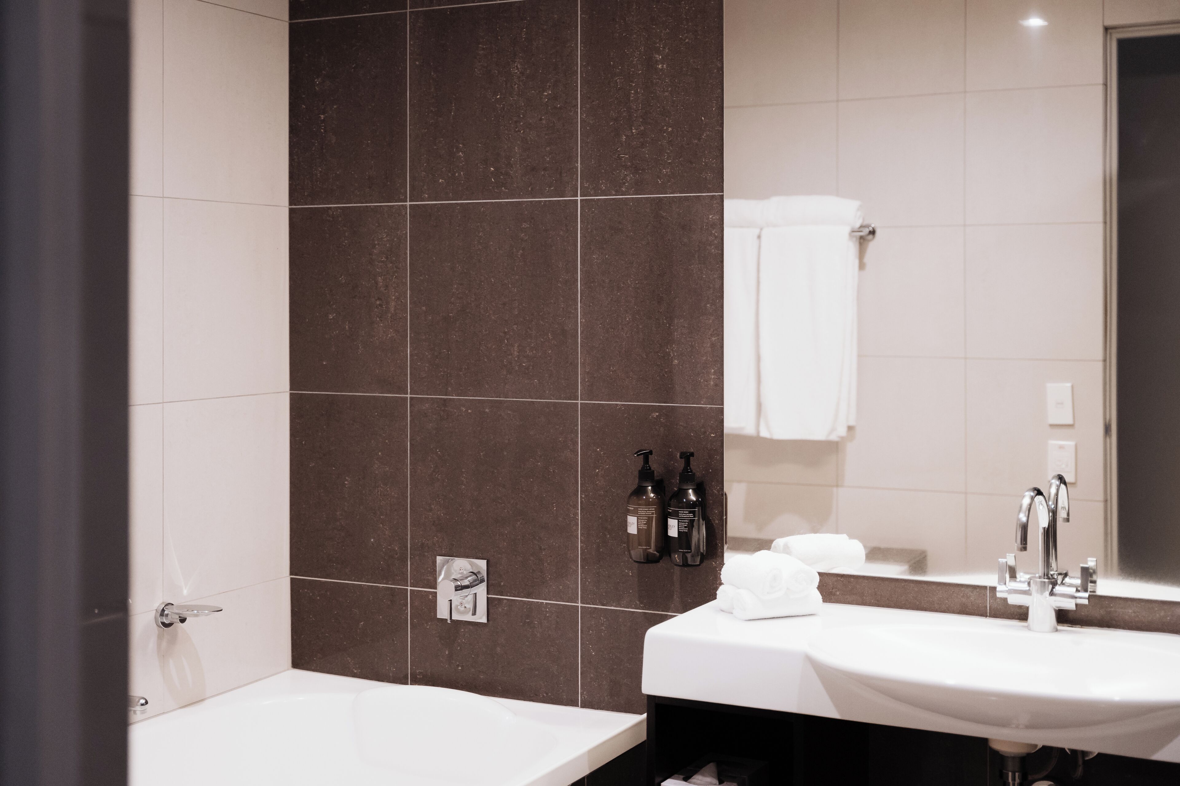 A modern bathroom with a white sink, dark brown tiles, and a mirror.