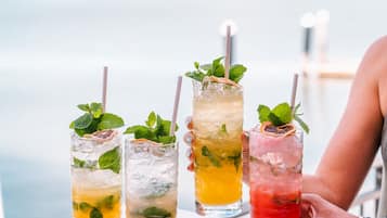 Quatre grands verres de boissons glacées, garnis de feuilles de menthe et accompagnés de pailles, disposés sur un plateau.
