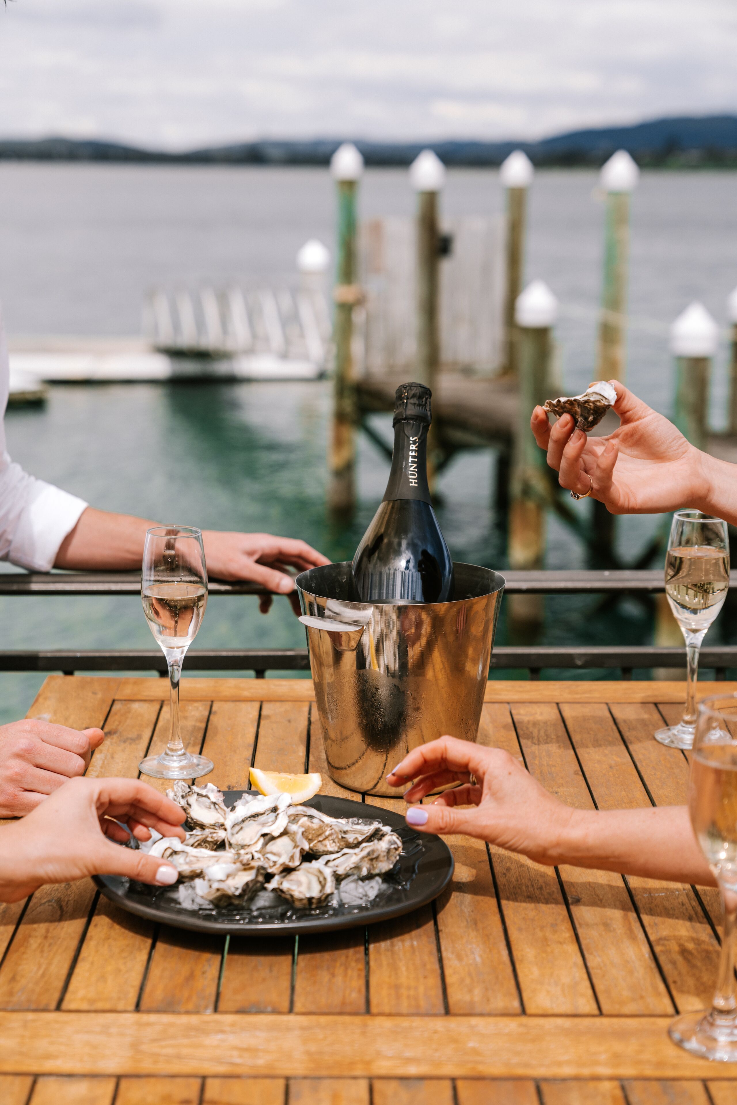 A wooden table with a bottle of wine, a plate of oysters, and glasses of wine.