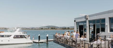 A waterfront dock with a white yacht and a building with large windows and a balcony.