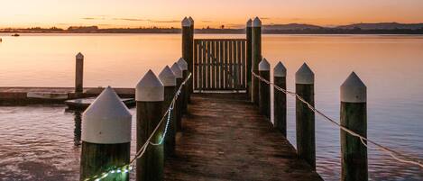 Un muelle de madera se extiende sobre aguas tranquilas con un atardecer al fondo.