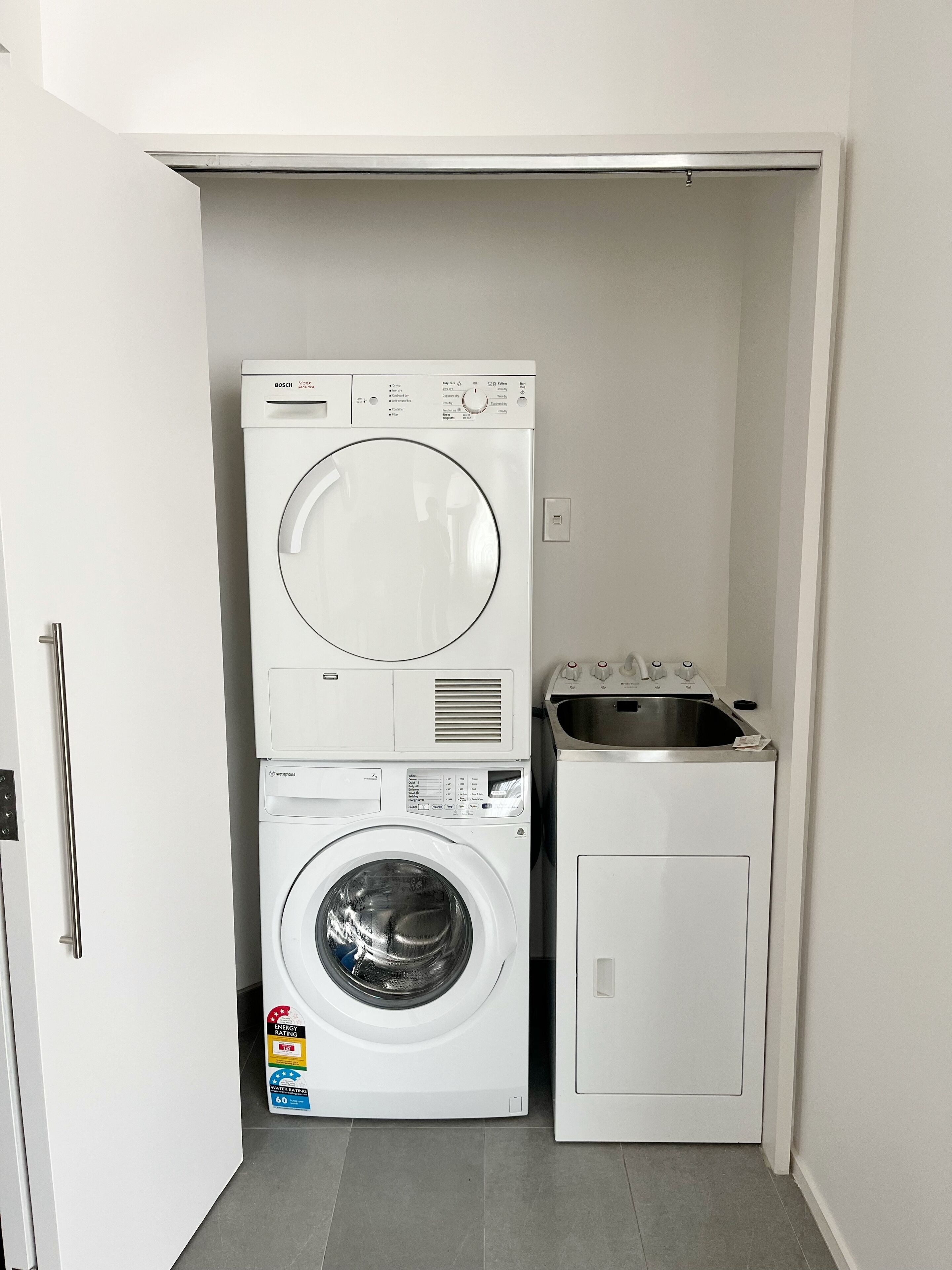 A compact laundry room with a stacked washer and dryer, a small sink, and a door.